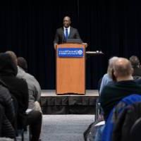 Man at podium with projection screens on either side